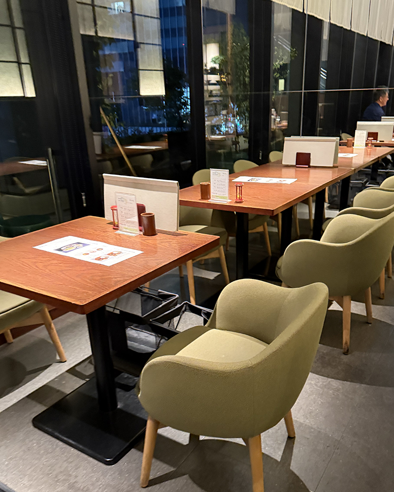 Interior of Fujii Meien. Chairs upholstered in tea colored fabric. Wooden tables and chair legs. Night outside the window.