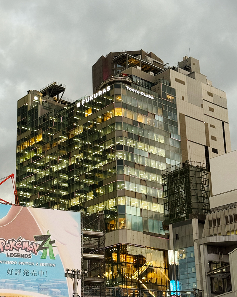View of the building Fukuras during rainy twilight. A tall building starting to show the lights shining against the background of a cloudy twilight.