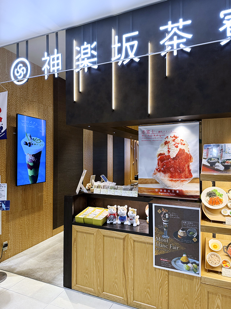 Exterior of Kagurazaka Saryo on the 14th floor. Neon white kanji above the entrance, light wood counters with food samples behind glass.