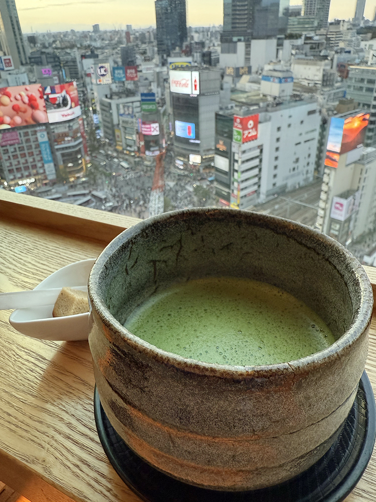 A tea bowl of matcha in front of a window looking over Shibuya intersection from the 14th floor.