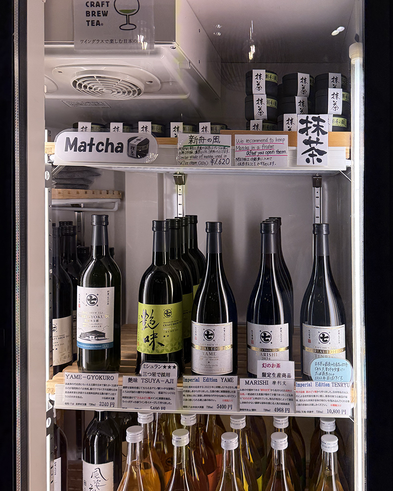 A store fridge with shelves of large bottles of craft tea. Mainly dark green bottles with various labels in Japanese.