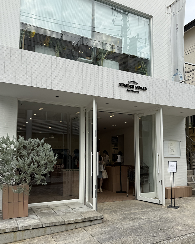External view of Number Sugar, a caramel shop. Concrete building, floor to ceiling windows, two doors wide open.