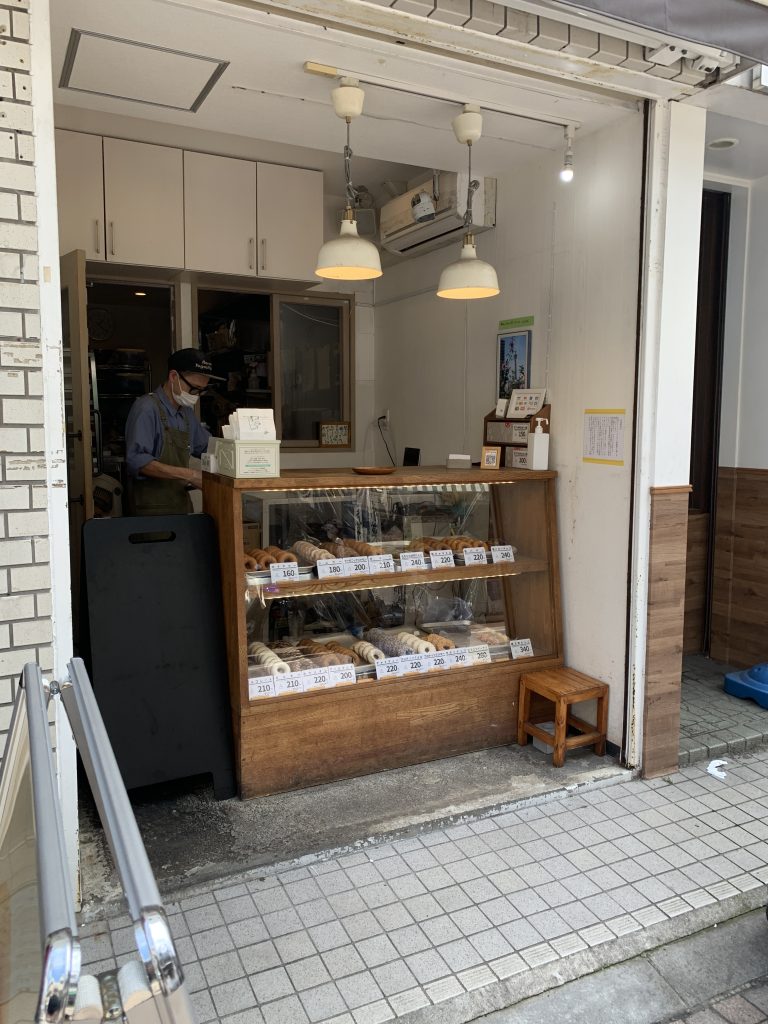 Exterior of the small take-out only location of the old Togoshi Ginza branch of Floresta donuts. Shop is a small alcove with traditional wood and glass case displaying different donut varieties.