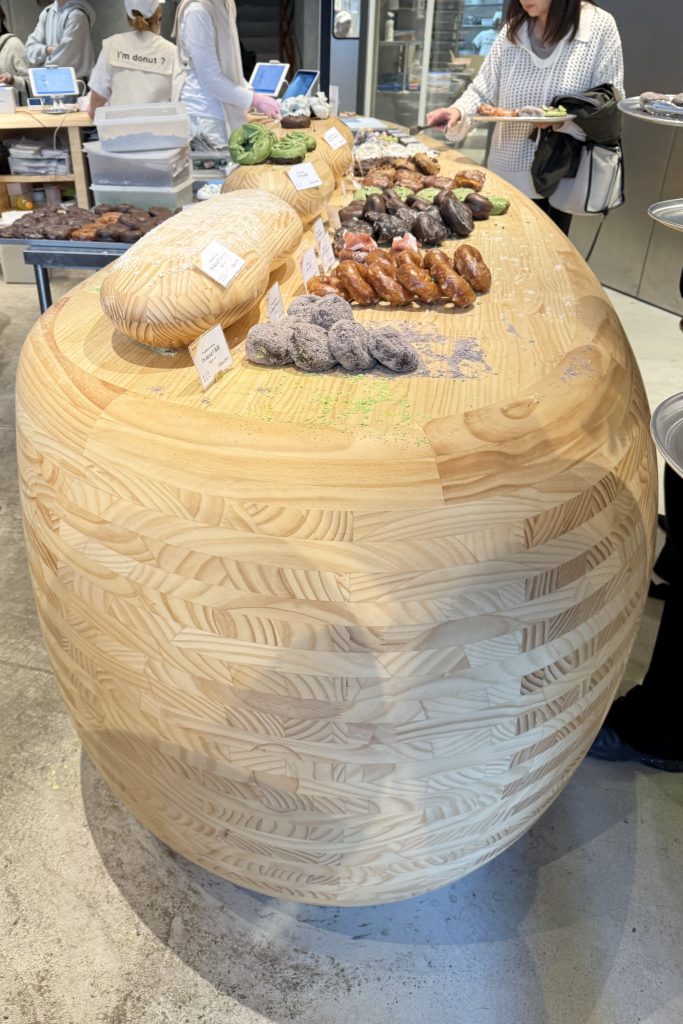 Organic, bean-shaped wooden counter displaying assorted donuts at I’m Donut in Jiyugaoka, Tokyo